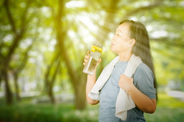 年配の女性が公園で運動した後に水を飲む