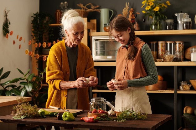 Senior woman explaining her granddaughter how to peel garlic for pickles