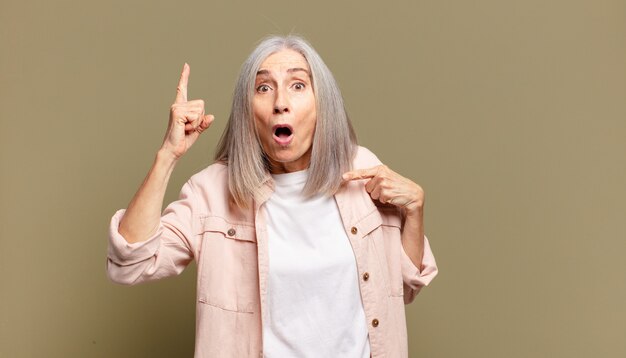 Senior woman feeling proud and surprised, pointing to self confidently, feeling like successful number one