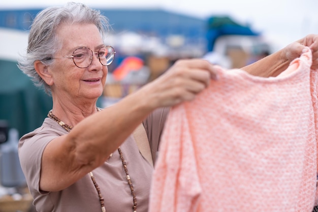 Пожилая женщина на блошином рынке ищет подержанную одежду, обувь, сумки, украшения, нулевые отходы, шопинг, экологически чистая концепция устойчивого образа жизни