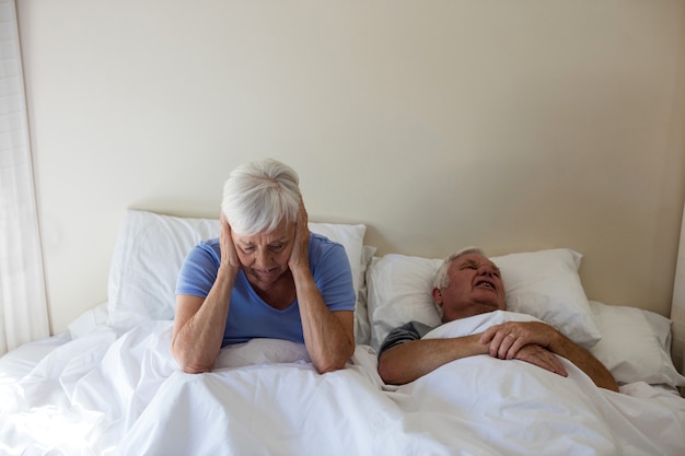 Senior woman getting disturbed with man snoring on bed in bedroom