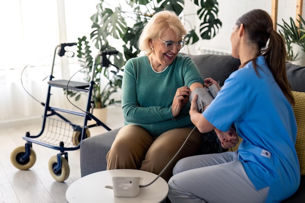 senior woman getting her blood pressure measured at nursing home female nurse teaching elderly woman to measure blood pressure at home senior woman visited by home care specialist