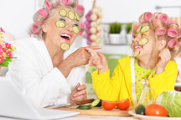 Senior woman and granddaughter at kitchen with  vegetables and laptop