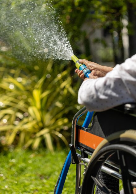 裏庭でホース噴霧器と散水植物を持っている年配の女性の手