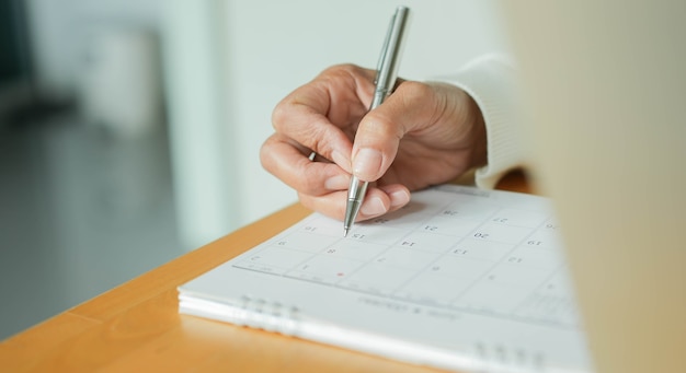 Mano della donna anziana che usa la penna per segnare o fissare un appuntamento sul calendario