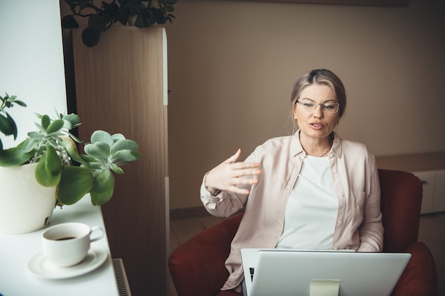 Senior donna che ha corsi in linea sul computer portatile e spiegare qualcosa che indossa gli occhiali durante il blocco