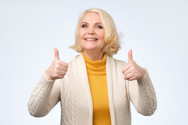 Senior woman in her 70s showing thumbs up gestures with both hands,