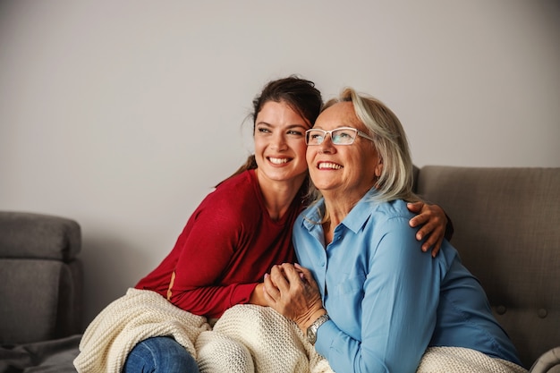 Senior woman and her daughter sitting at home and hugging.