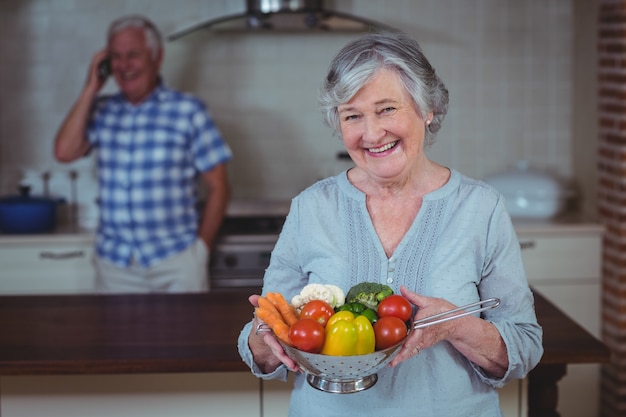 Senior woman holding colander with vegetables