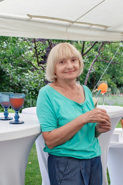 夏の裏庭の退職パーティー中にカラフルな飲み物のグラスを保持している年配の女性