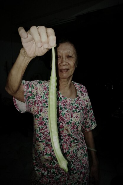 Senior woman holding long okra at night