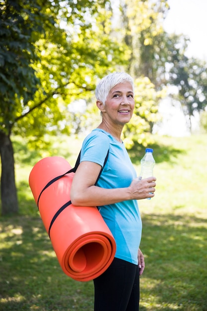 Photo senior woman holds fitness mat on her back in the park