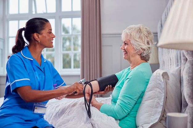 Photo senior woman at home in bed having blood pressure taken by female care worker in uniform