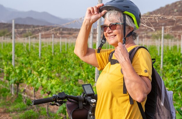 Donna anziana all'interno di un vigneto con la sua bici elettrica, godendosi all'aperto e la natura