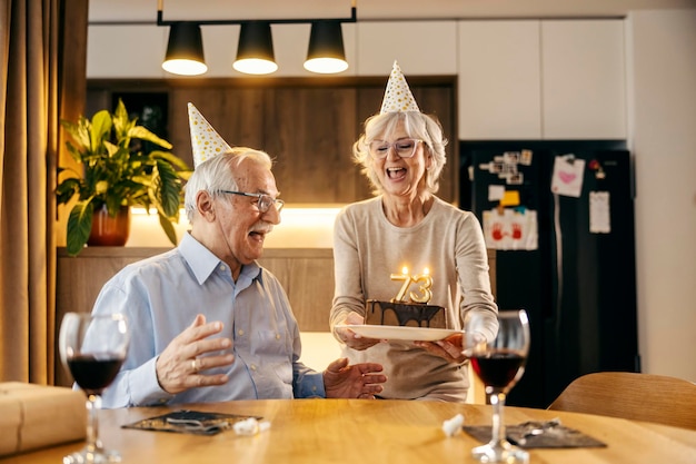 한 고령 여성이 남편에게 생일 케이크를 가져오고 있습니다.