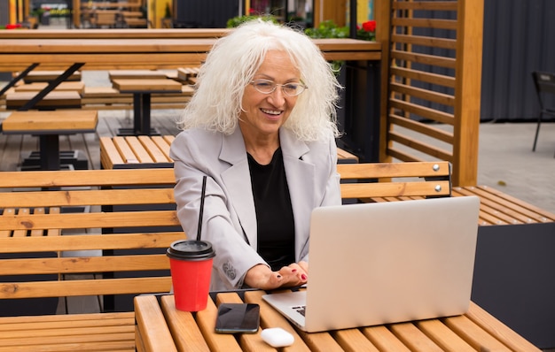 Photo senior woman is resting in a cafe in the fresh air communicates using true wireless video