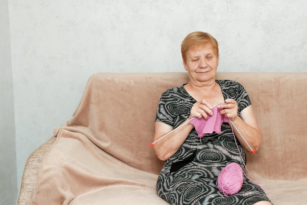 senior woman knitting sitting at home on the sofa