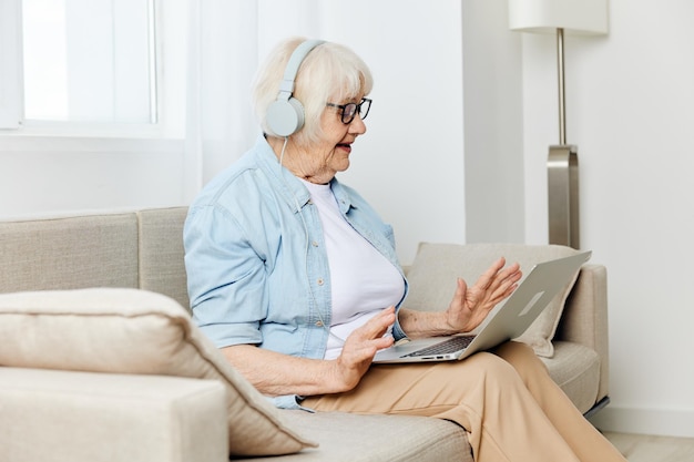 senior woman listening music through headphones sitting with laptop at home