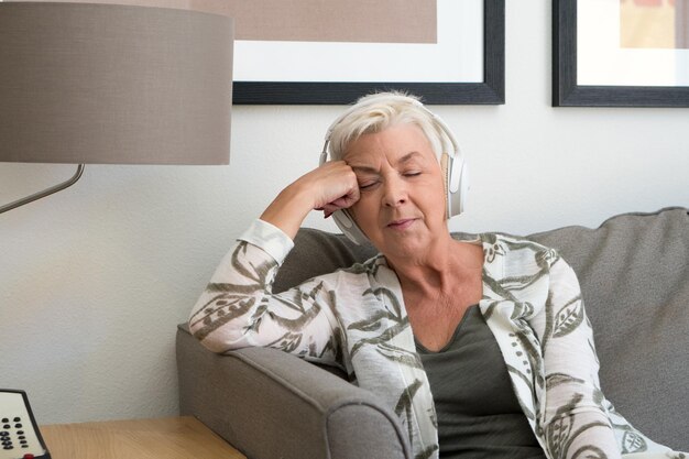 Photo senior woman listening music while sitting on sofa at home