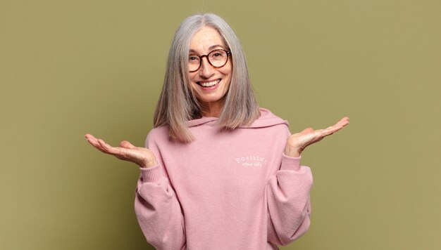 Senior woman looking happy and excited, shocked with an unexpected surprise with both hands open next to face