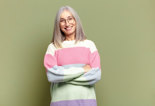 Senior woman looking like a happy, proud and satisfied achiever smiling with arms crossed