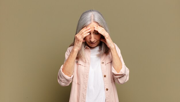 Senior donna che sembra stressata e frustrata, lavora sotto pressione con un mal di testa e turbata da problemi