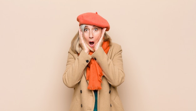 Senior woman looking unpleasantly shocked, scared or worried, mouth wide open and covering both ears with hands