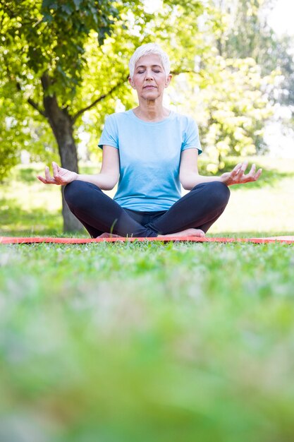 Senior woman in lotus pose sitting on green grass