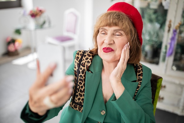 카페에서 즐거운 시간을 보내는 스마트폰을 사용하여 셀카를 만드는 노인 여성