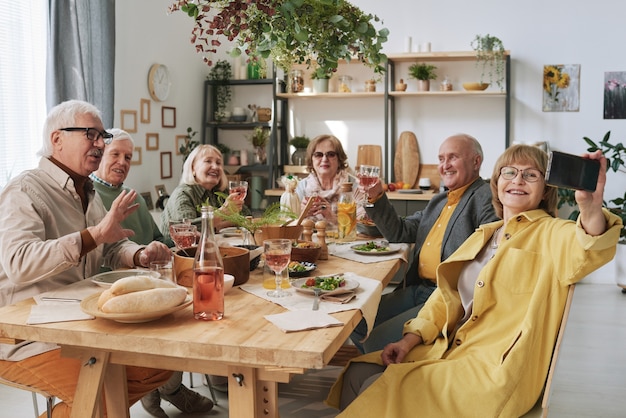 Senior woman making selfie with her old friends on mobile phone while they sitting at the table during dinner