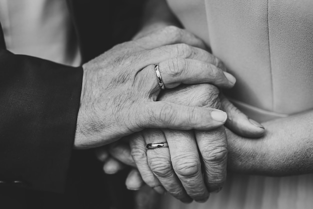Senior woman and man hold hands with each other retirement life\
elderly community concept closeup elderly couple together outdoors\
focus on hands close up black and white photo