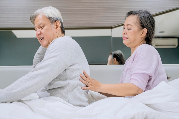 Senior woman massaging of her back husband on bed