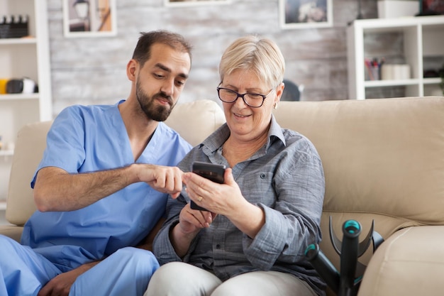 Photo senior woman in nursing home getting help from young doctor to use her phone.