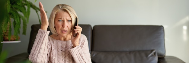 Senior woman in a phone call sitting on a sofa in the living room in a house