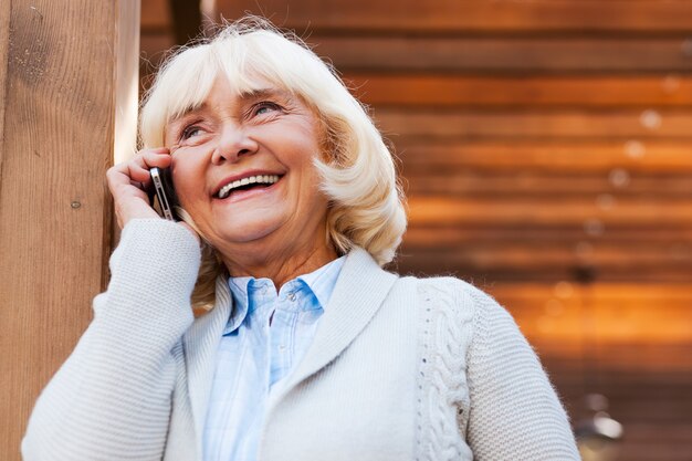 Старшая женщина по телефону. Счастливая старшая женщина разговаривает по мобильному телефону и улыбается, стоя на открытом воздухе