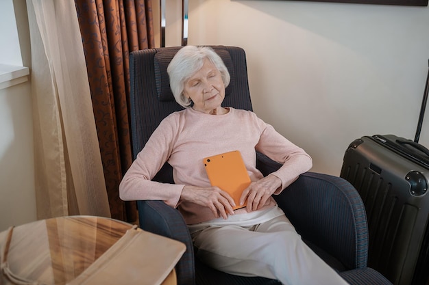 A senior woman in pink blouse with a tablet sitting in an armchair