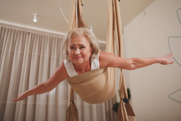 Senior woman practicing aerial yoga at sport studio