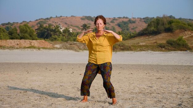 Senior donna pratica ginnastica taiji in spiaggia sabbiosa