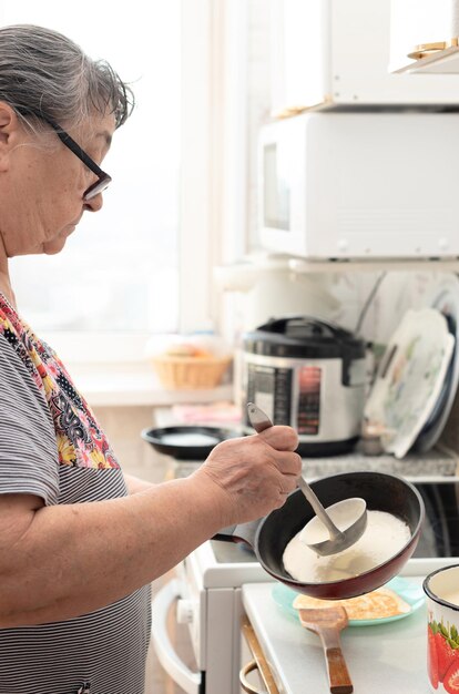 Senior woman prepares delicious pancakes in the kitchen in the morning for tasty breakfast