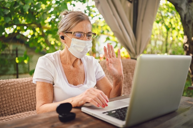 Senior woman in protective face mask using laptop
