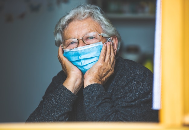 Donna anziana messa in quarantena dal coronavirus, covid-2019 in una casa, guardando fuori dalla finestra