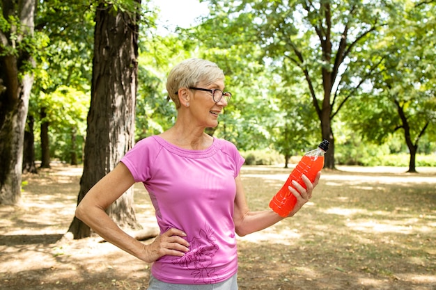 Senior donna pronta per l'allenamento tenendo la bevanda energetica nel parco.