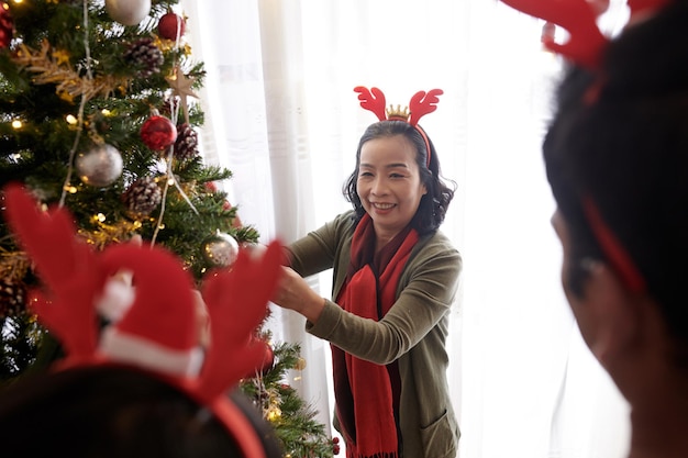 Senior donna in corna di renna archetto godendo di decorare l'albero di natale a casa