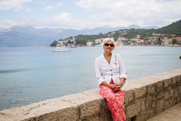 Senior Woman Relaxing by the sea on the seashore. Happy elderly woman of 70 years enjoing on the trip. Vacation travel concept.