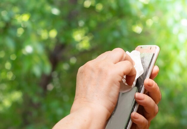 Senior woman's hand is spraying alcohol, spraying disinfectant spray on mobile phone