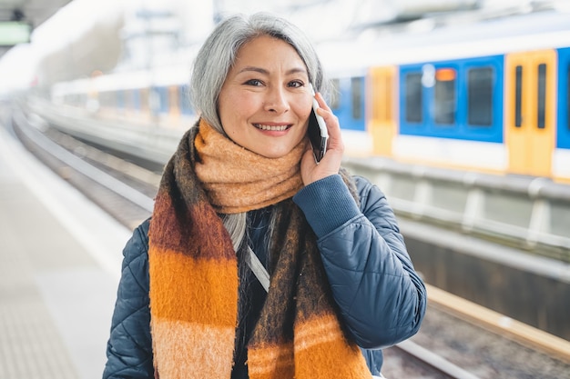 La donna senior invia un messaggio con un telefono cellulare e aspetta un treno