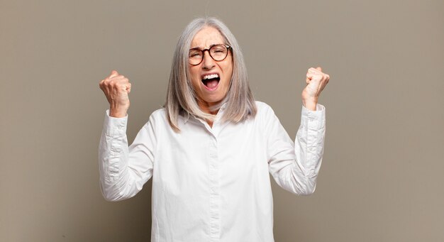 Senior woman shouting aggressively with an angry expression or with fists clenched celebrating success