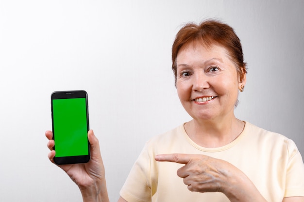 La donna senior mostra un telefono su bianco in una maglietta leggera