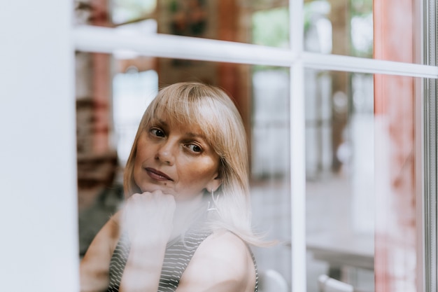 Senior woman sits in front of the window mature adult woman looking sad and thoughtful mental health