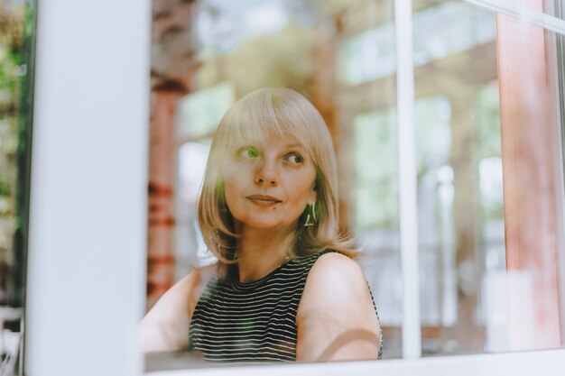 Senior woman sits in front of the window mature adult woman looking sad and thoughtful mental health